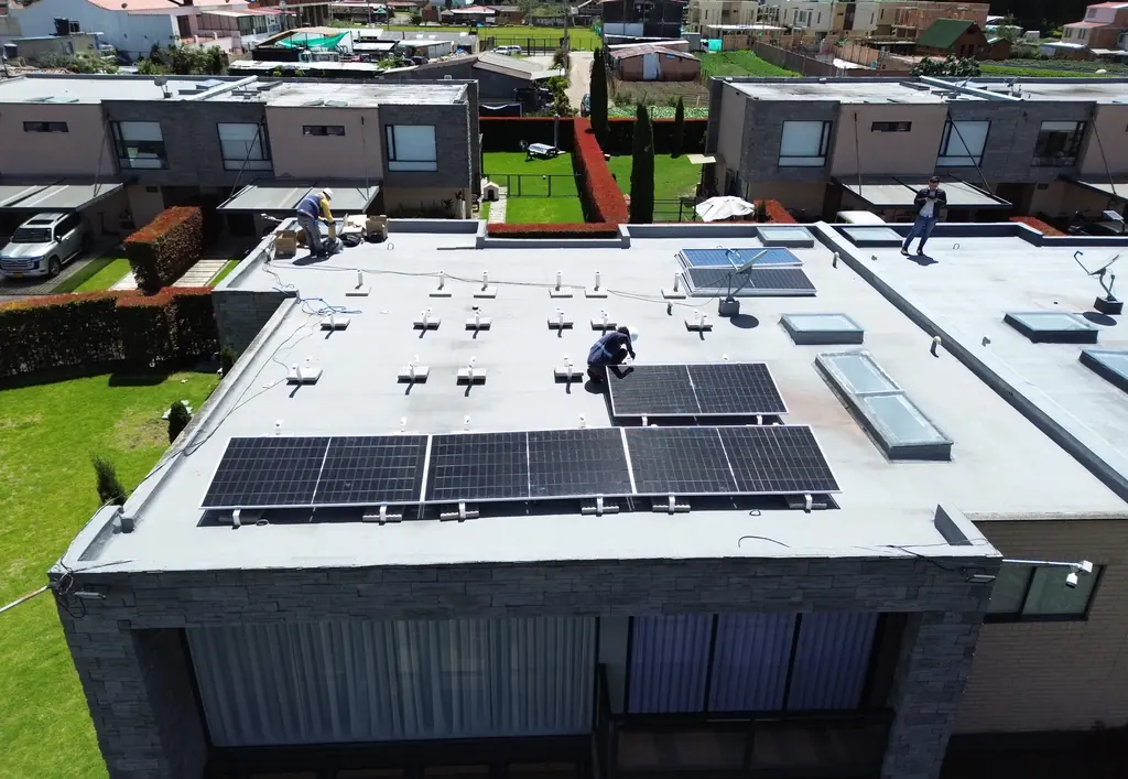 Vista de dron de la casa 51 del condominio Serrato en Cota, con una fila de módulos solares en el borde del techo y técnicos trabajando.