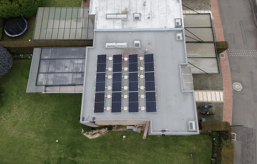 Vista cenital de dron de la casa 54 del condominio Serrato: filas de módulos solares sobre estructura con lastre en un techo plano, junto a un patio con cubierta de vidrio.